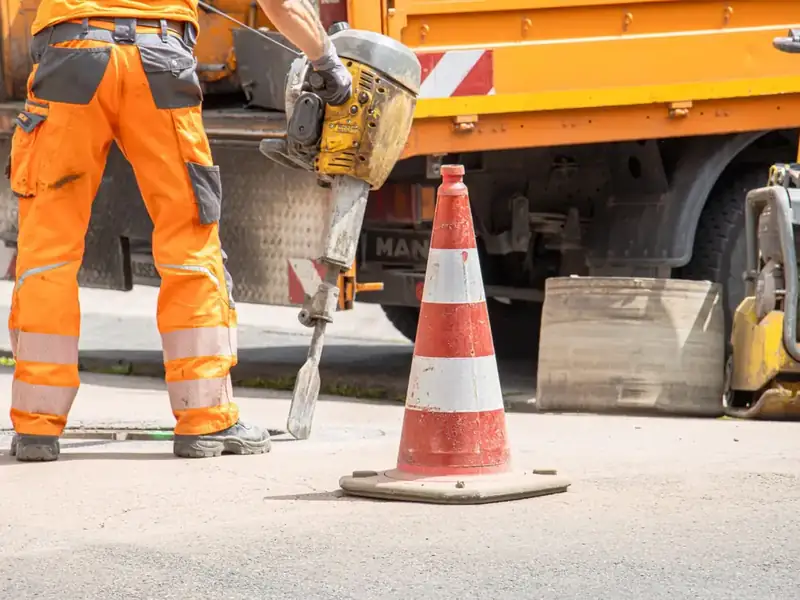 A municipal worker in high-visibility clothing repairing a road with a jackhammer