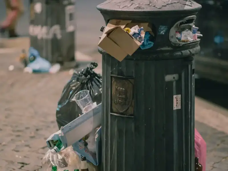 An overflowing public waste bin surrounded by litter